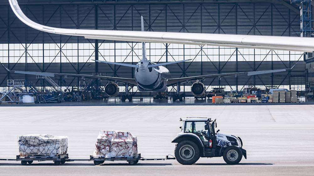 Cargo tractor driving past airplane hanger